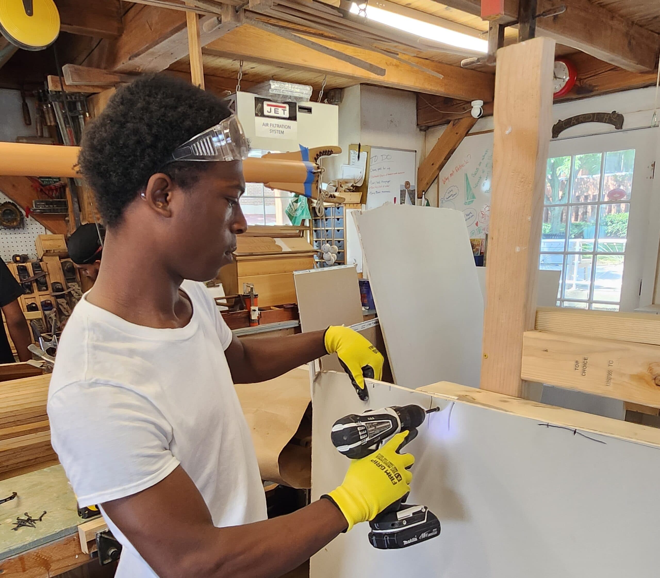 Three students in hard hats and safety vests measuring and fastening wall framing together